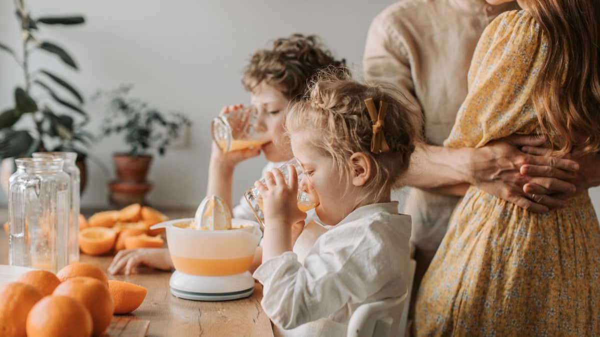 A loving family moment with children drinking fresh orange juice indoors.